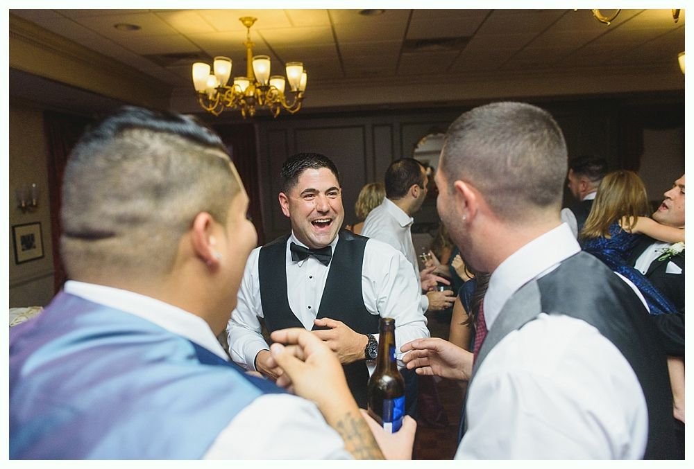 Three men in formal attire laughing, possibly at a wedding reception.