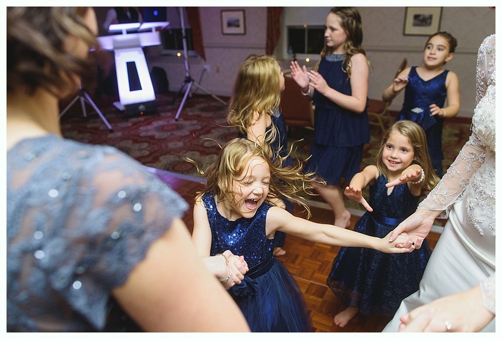 Girls in navy dresses dance joyfully on a wooden dance floor at a party.