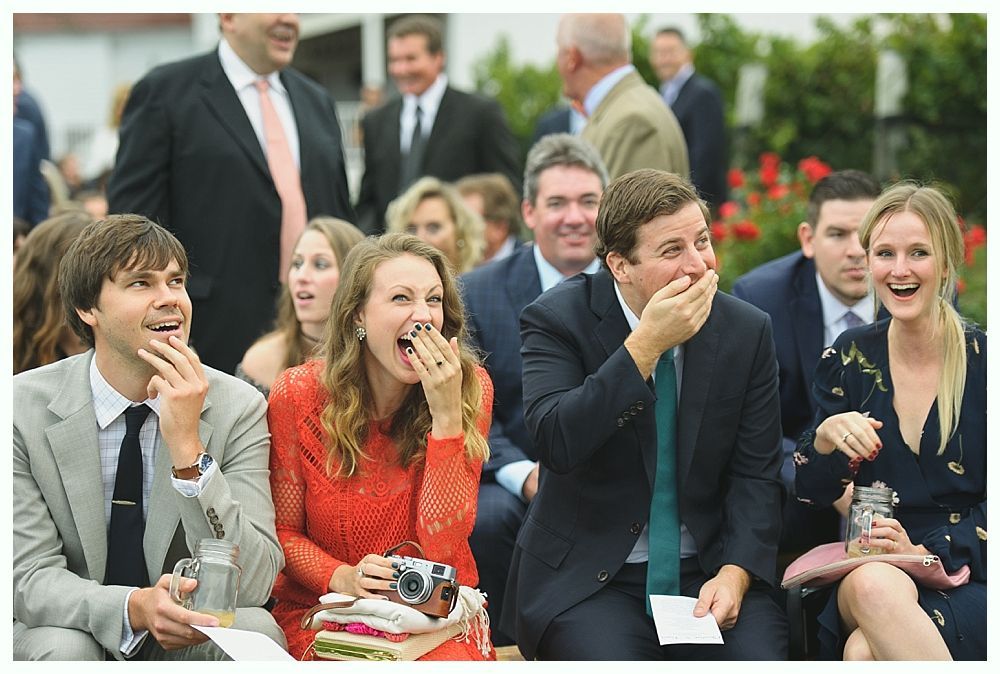 People laugh at outdoor event; woman in red dress yawns, man covers mouth, others watch.