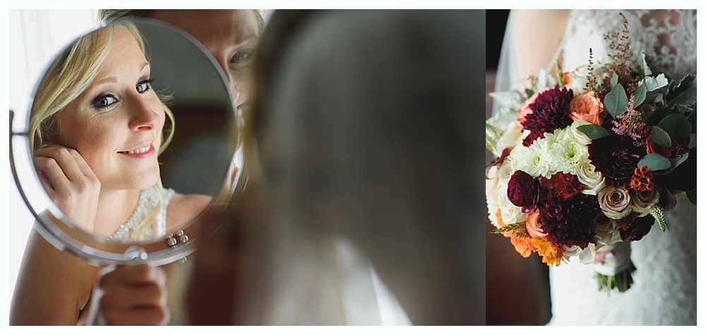 Bride puts on earrings in a mirror, holding a bouquet.