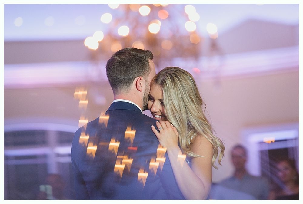 Couple embracing and dancing, blurred bokeh lights in background, likely at a wedding reception.