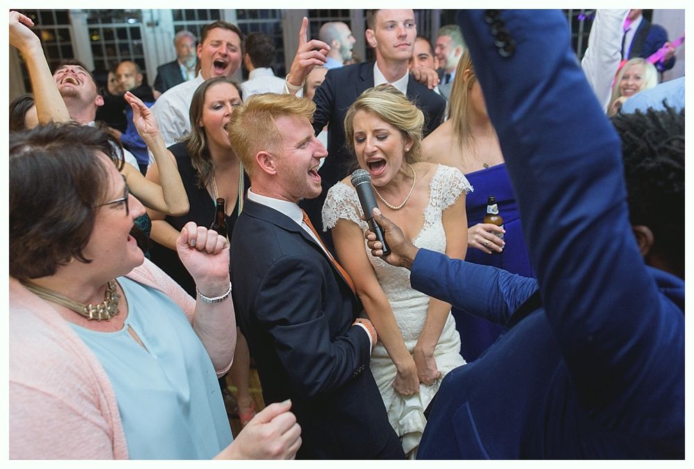 Wedding reception: Bride and groom sing into a microphone, surrounded by excited guests.