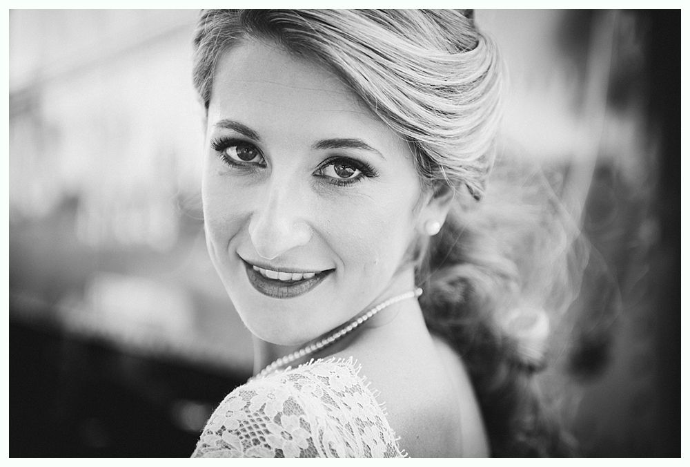 Woman with braided hair, smiling over her shoulder, wearing a pearl necklace and lace dress.
