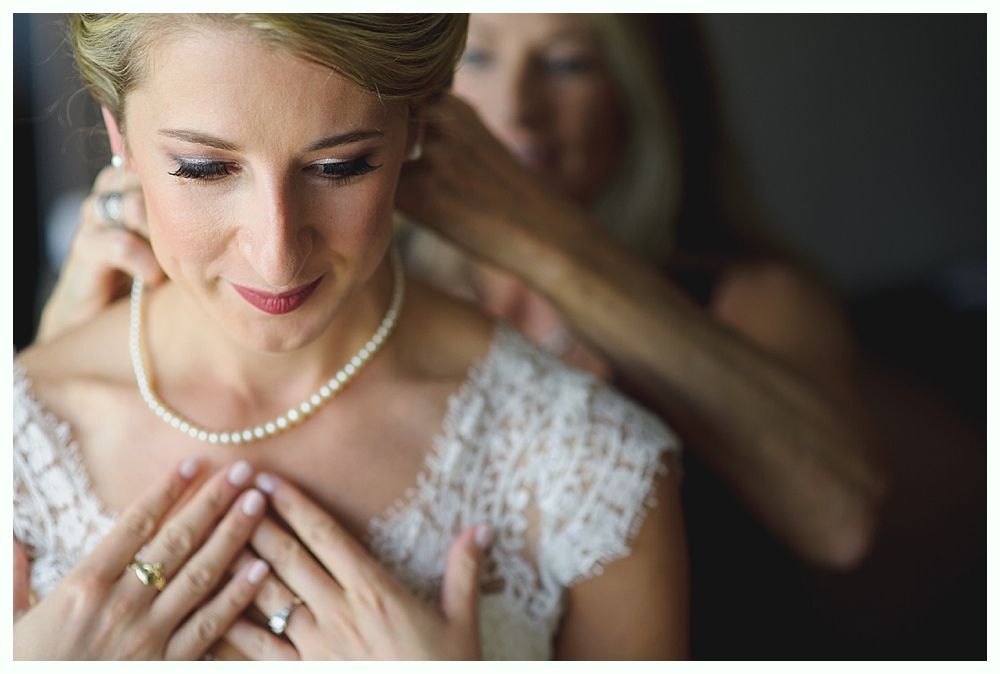 Bride in lace dress getting pearl necklace from person.