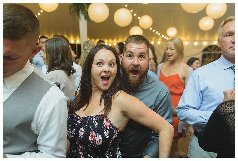 A woman and a man with surprised expressions posing at a party under string lights.