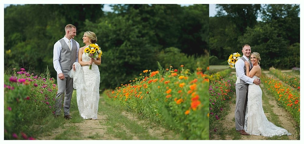 Bride and groom in wedding attire pose in a flower field, the woman holding a bouquet.