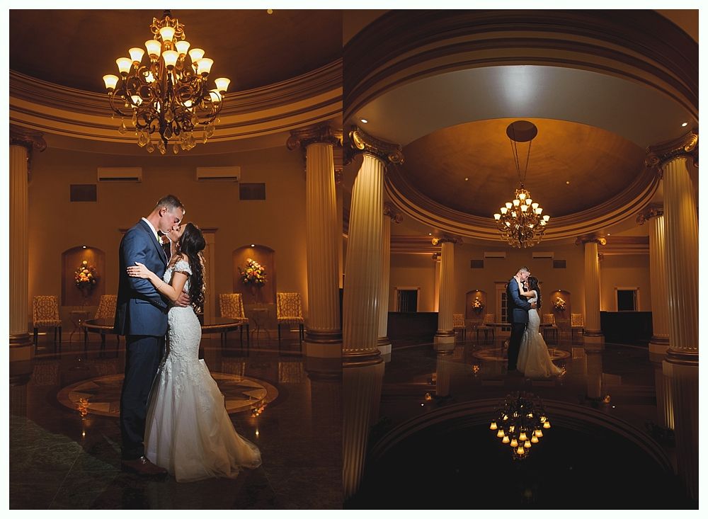 Couple in formal wear kissing under a chandelier in an ornate ballroom.
