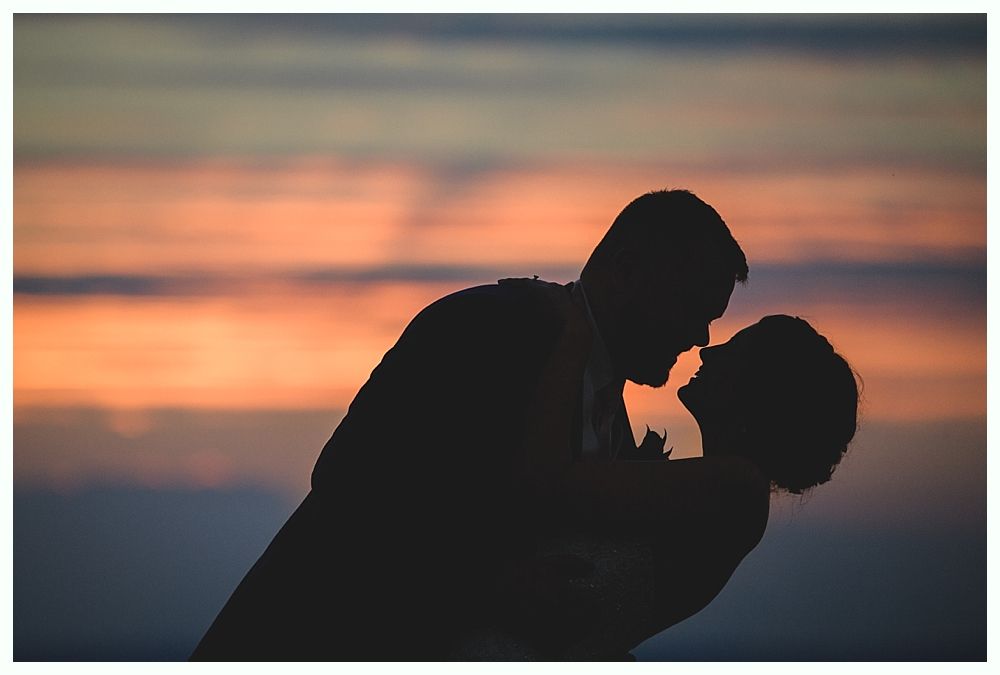 Silhouette of a couple kissing, against a colorful sunset sky.
