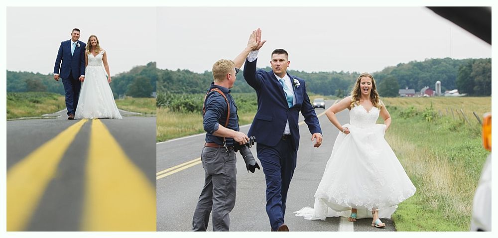 Newlyweds high-five on a road with their photographer; the bride smiles as she stands on the road.