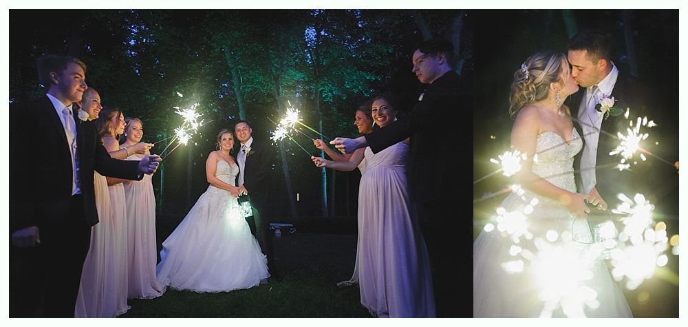 Wedding party with sparklers at night, bride and groom kissing, surrounded by attendants.