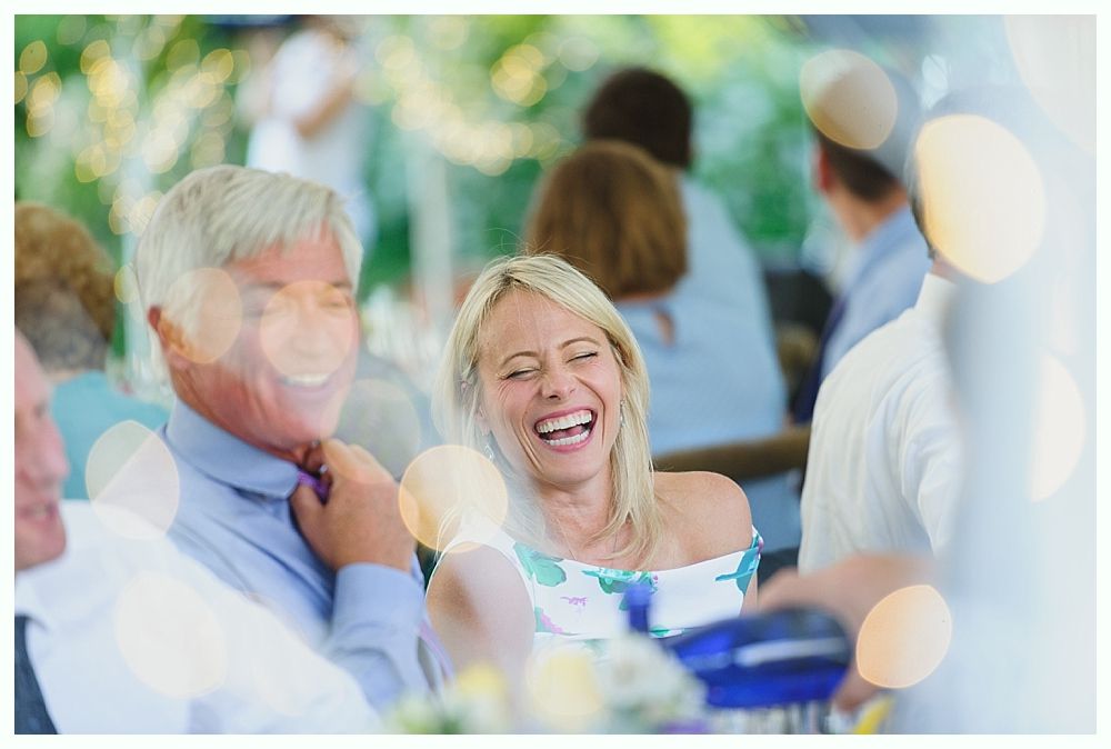 Bride and groom pose with a fire truck. The bride holds an axe, the groom flowers. Outdoors.