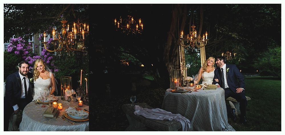 Couple at candlelit wedding reception, seated at table outdoors, under chandeliers.