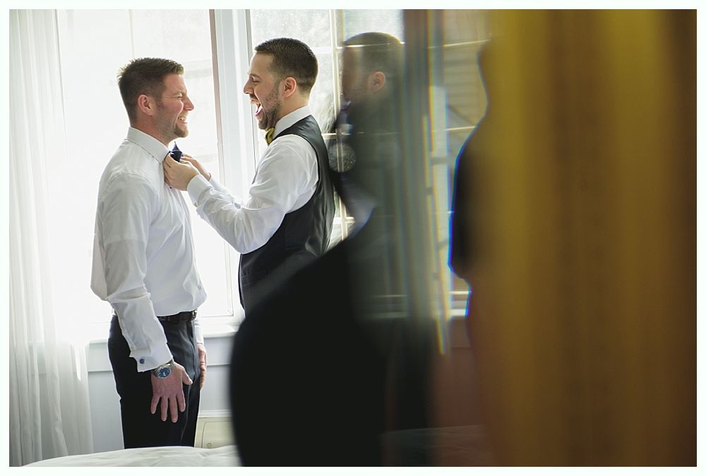 Two men, one adjusting the other's tie. They're in a well-lit room, possibly getting ready for a wedding.
