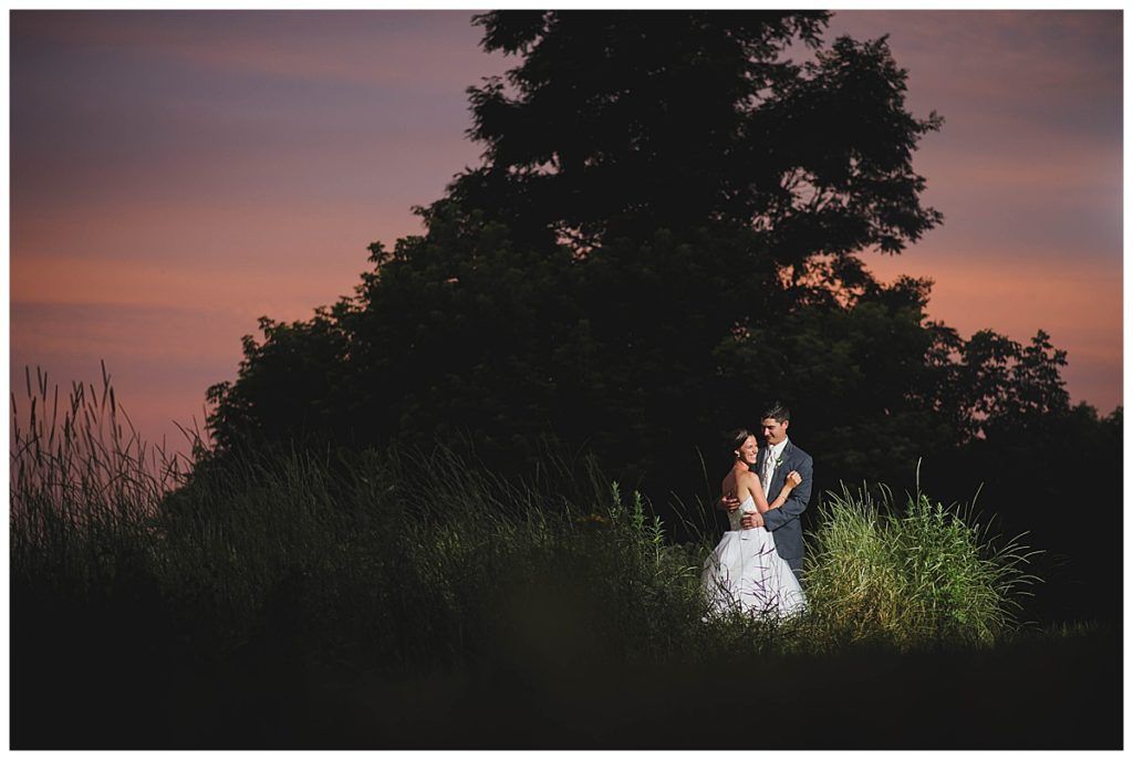 Couple embraces in a field at sunset, illuminated by a spotlight.