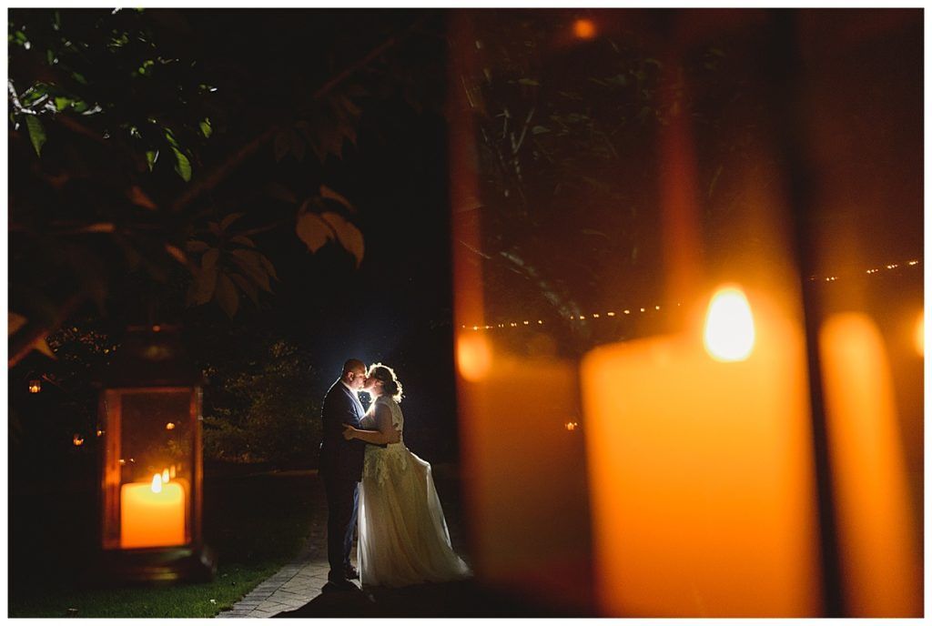 Couple embracing at night, lit by candles and lanterns, romantic wedding setting.
