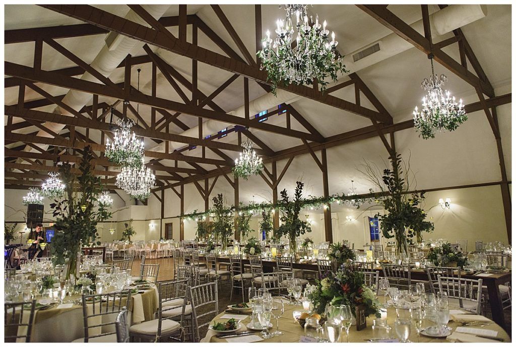 Elegant reception hall with tables set for a banquet; chandeliers and floral arrangements adorn the space.