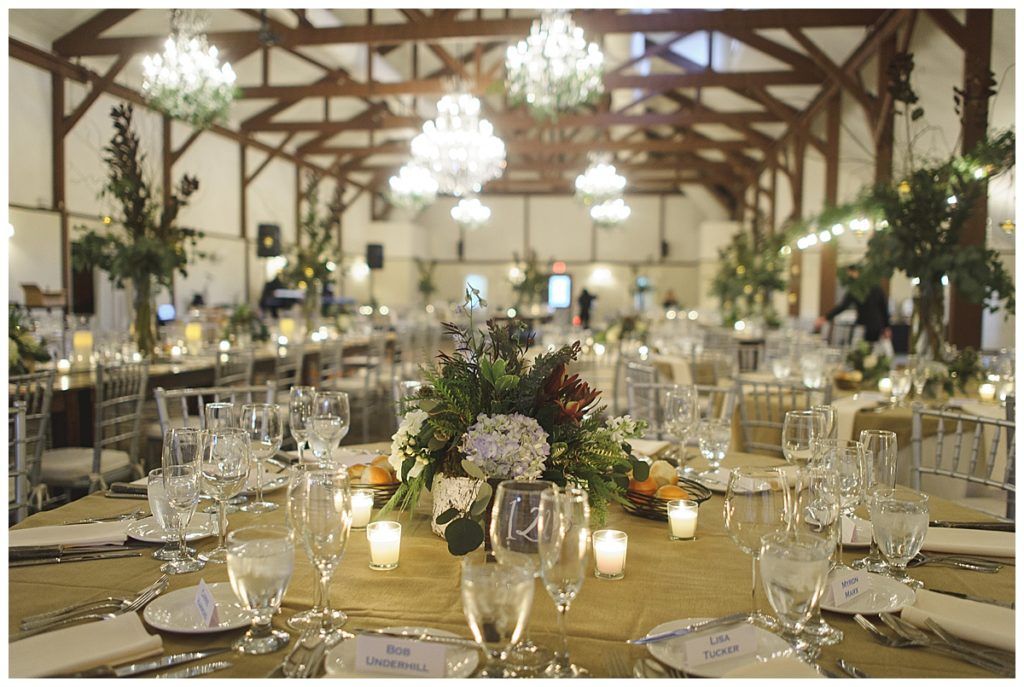 Elegant event space with decorated tables, chandeliers, and wooden beams overhead.