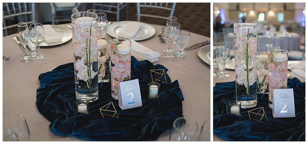 Wedding table setting with floral centerpiece in clear vases on navy blue fabric.