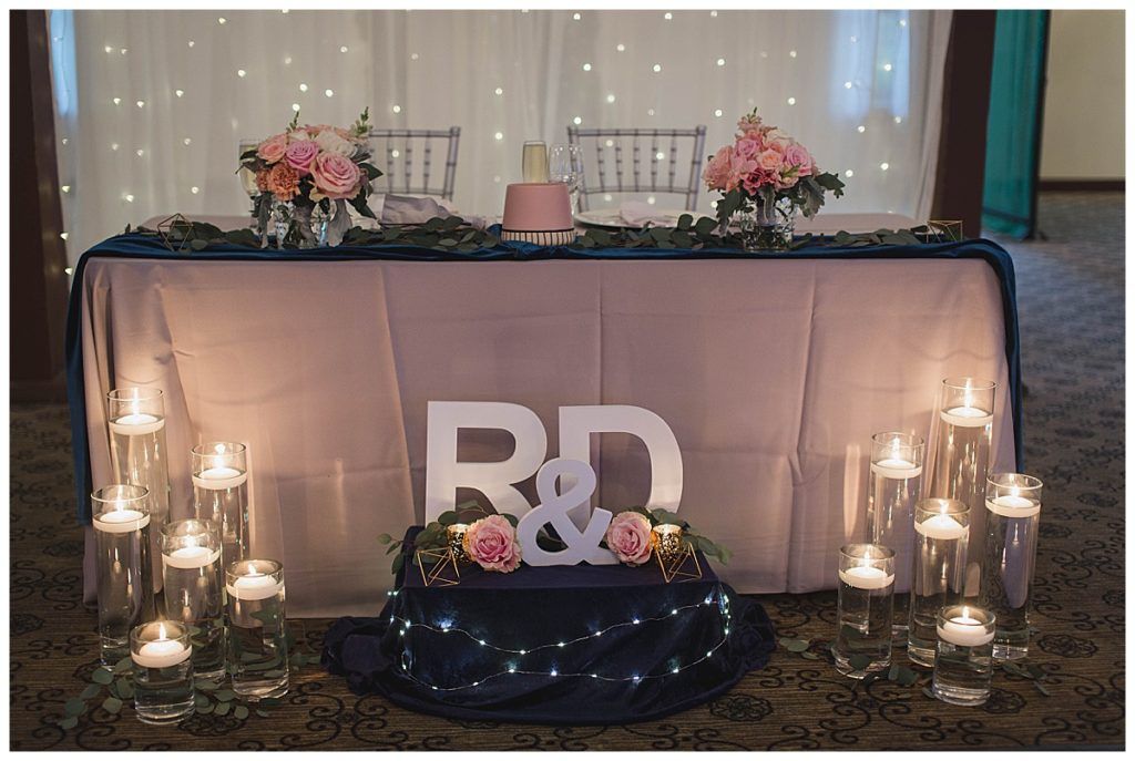 Wedding reception sweetheart table with flowers, cake, candles, and monogram letters 