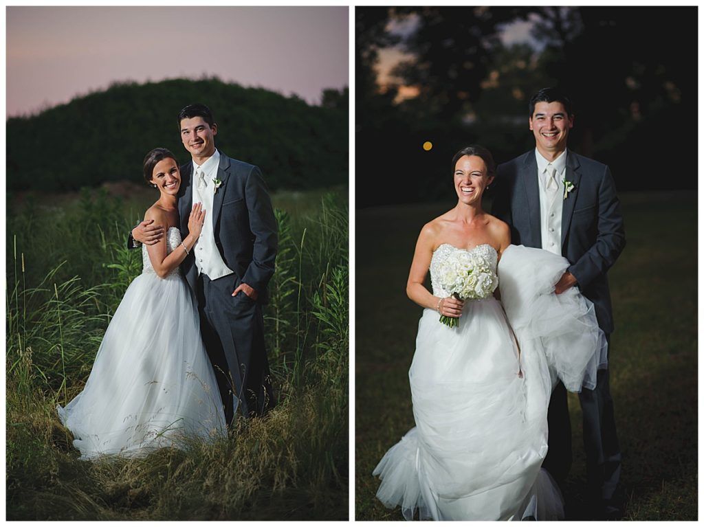 Wedding couple posing outdoors. Woman in white dress, man in gray suit. Grinning in a grassy field.