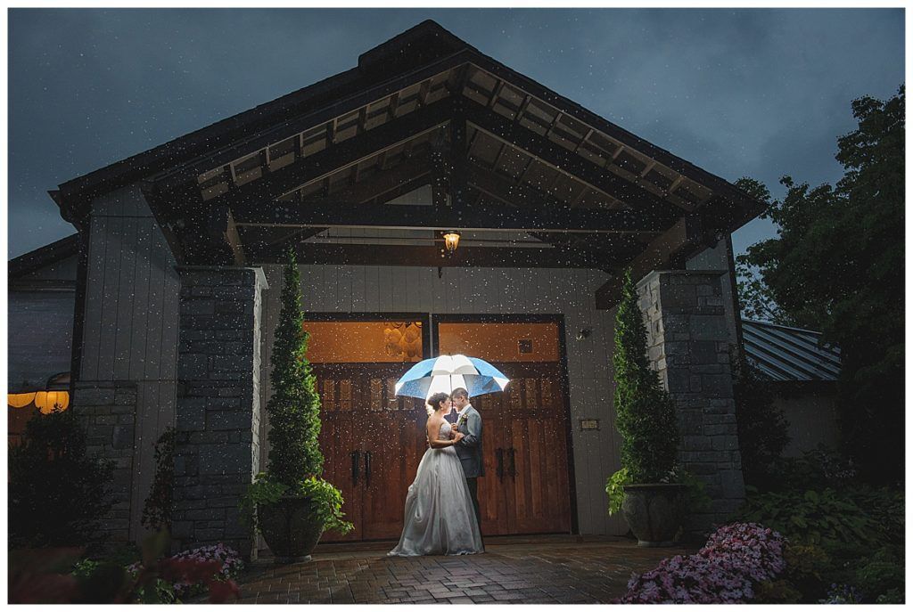 Couple under umbrella kissing in front of a building with rain falling.