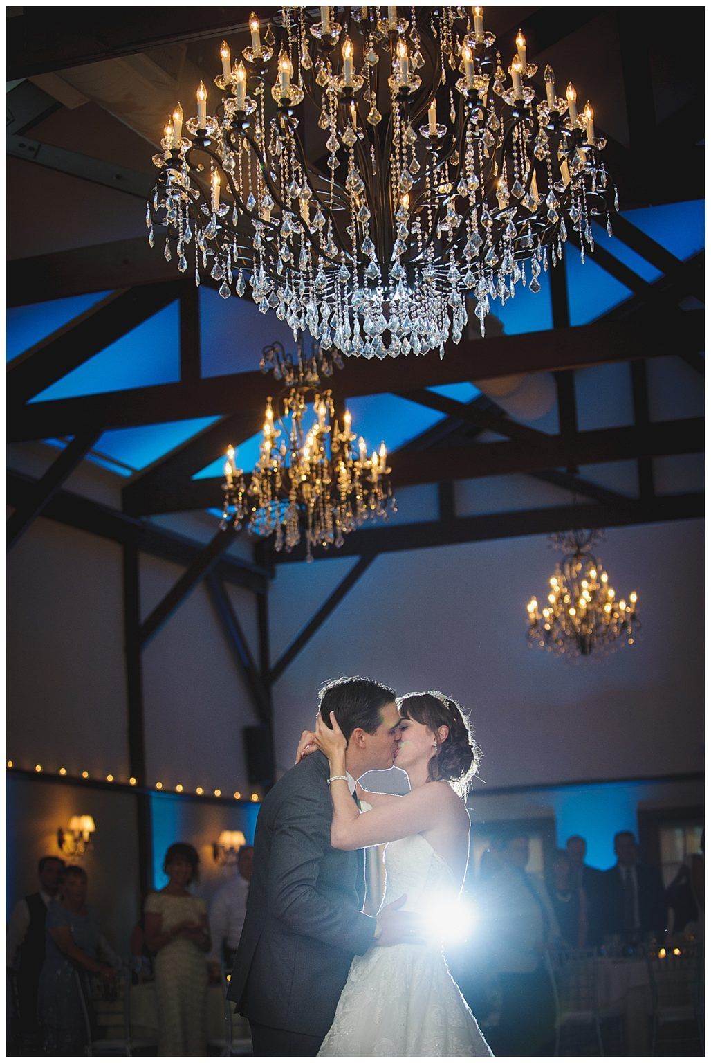 Couple kissing on a dance floor under chandeliers. Dark room, blue up-lighting.