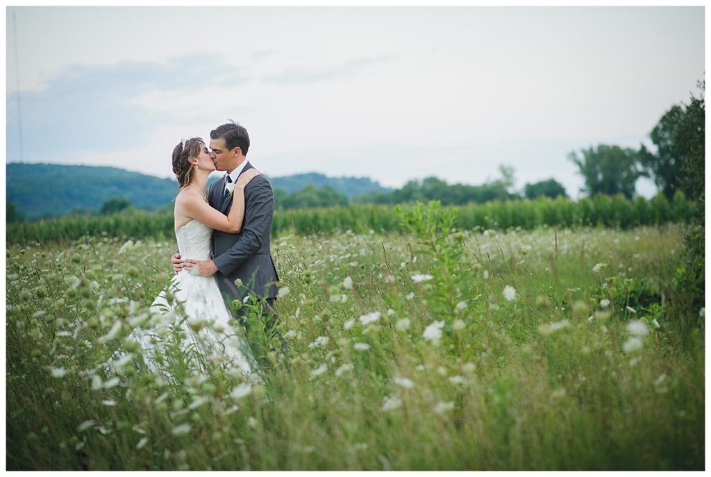 Bride and groom kissing in a field of wildflowers. Overcast sky.