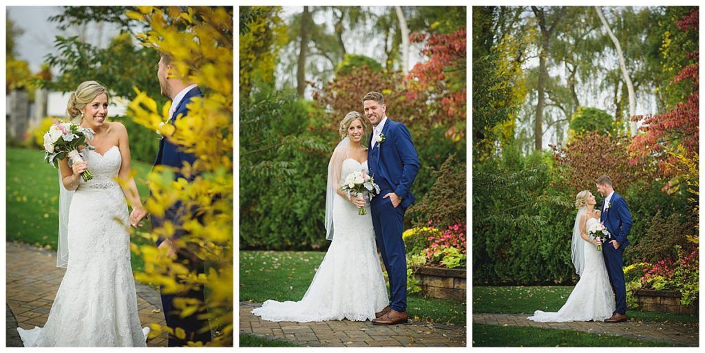 A bride and groom pose for photos in a garden. The woman smiles, the man wears a blue suit.