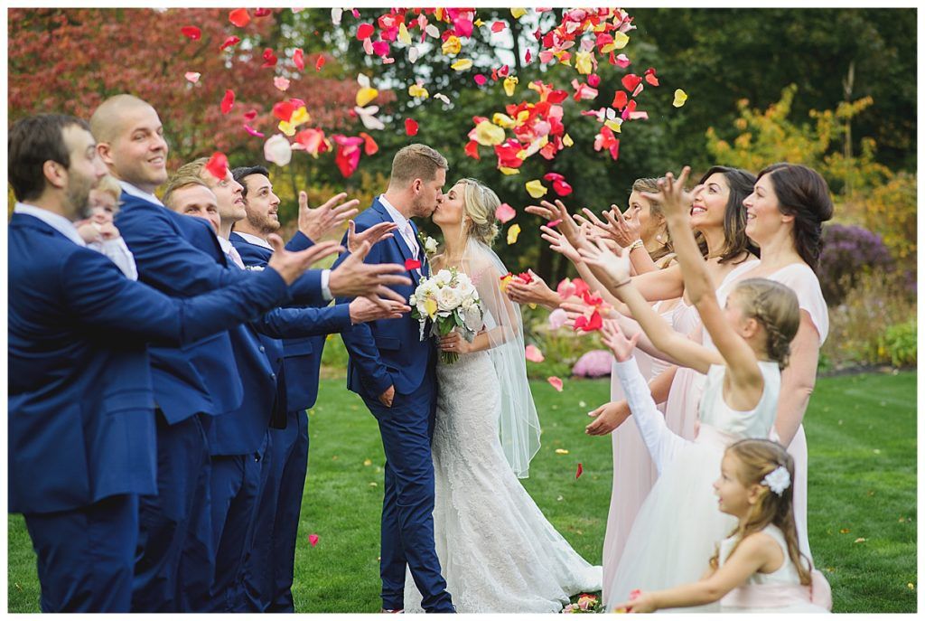 Wedding party celebrates couple with flower petals in a garden.