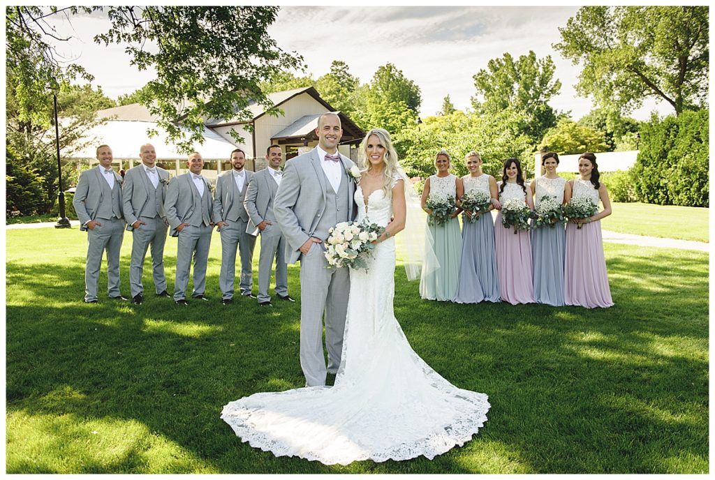 Bride and groom with wedding party on a lawn. Groom in gray suit, bride in white dress, bridesmaids in pastels, groomsmen in gray.