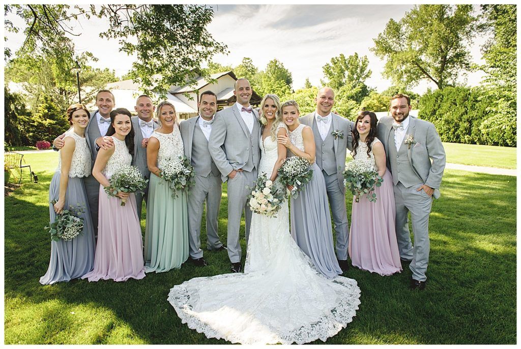 Wedding party in gray suits and pastel dresses posing on grass.