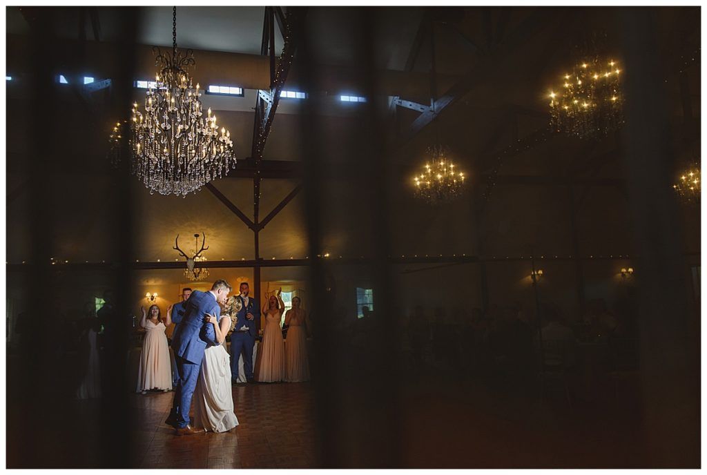 Couple dancing at a wedding reception, chandeliers overhead, guests watching.