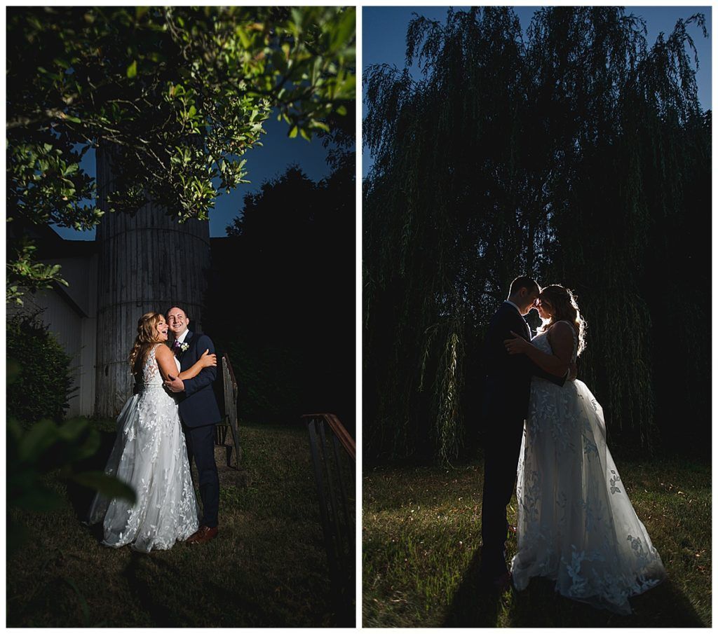Couple embracing, illuminated by a light, in wedding attire outdoors. Dark night setting, tree in background.