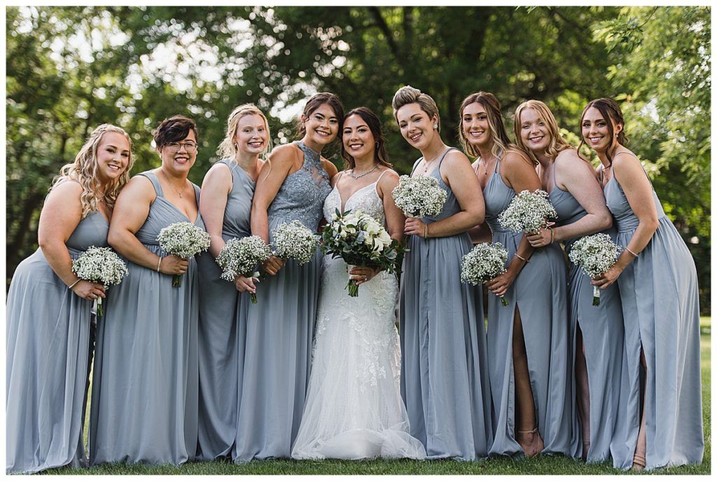 Bride with bridesmaids in blue dresses, holding bouquets, outdoors.