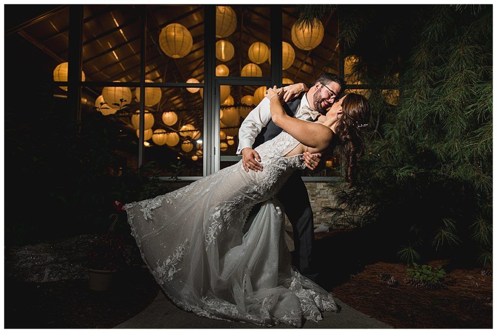 Bride and groom in formal attire, kissing while the groom dips the bride. Lanterns in background.