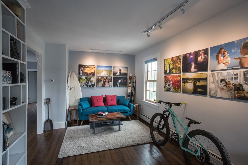A living room with blue couch, photos on wall, and a bicycle. Hardwood floors and white bookshelves are visible.
