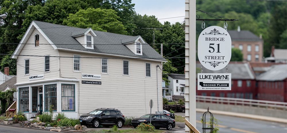 Bride and groom embrace on rocks by the ocean at sunset. The groom wears a blue suit, the bride a white dress.