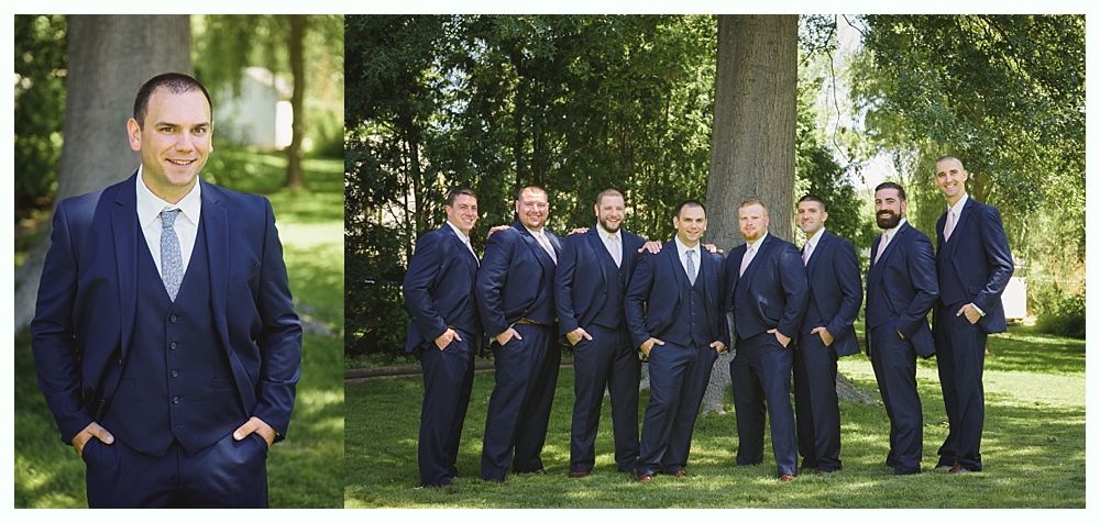 Nine men in matching navy suits pose outdoors, some smiling.