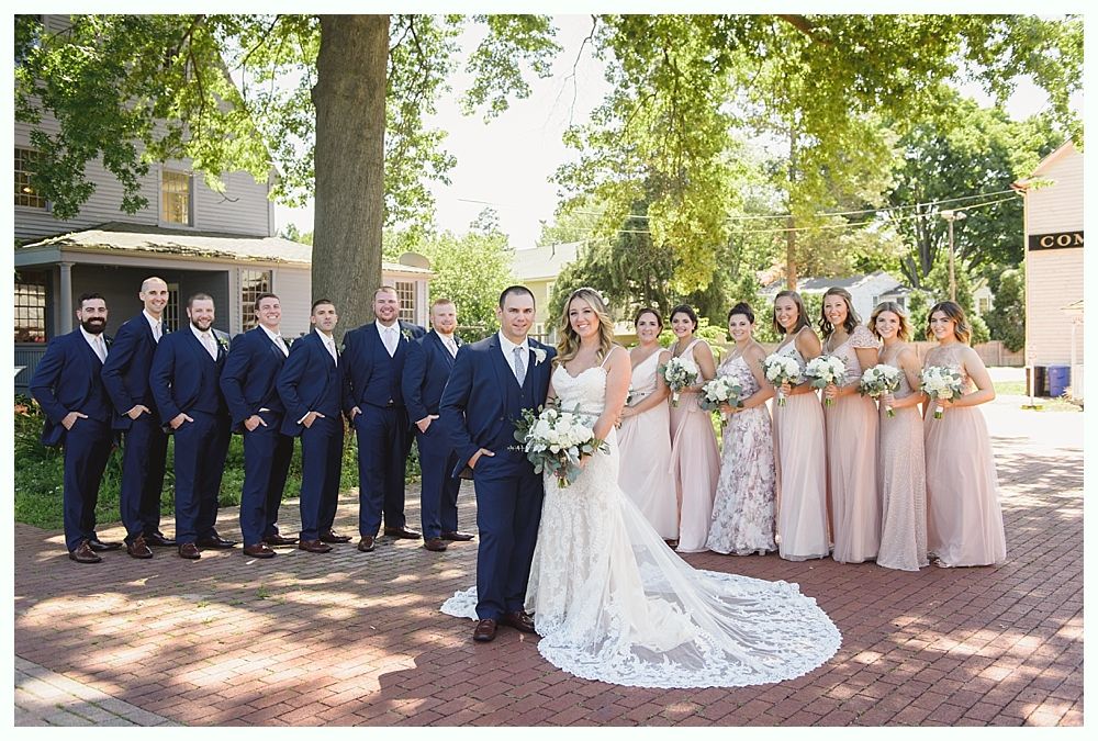 Wedding party posing outdoors. Bride and groom in center, bridesmaids in pink, groomsmen in navy.