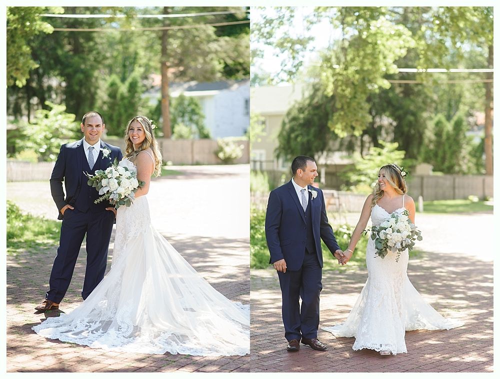 Wedding couple: Groom in navy suit and bride in white lace dress, holding hands, posing outdoors.