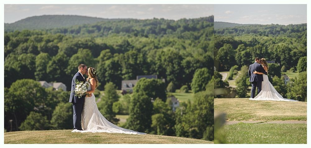 Couple kissing on a hilltop overlooking a green forest. The bride wears a white dress with a long train.