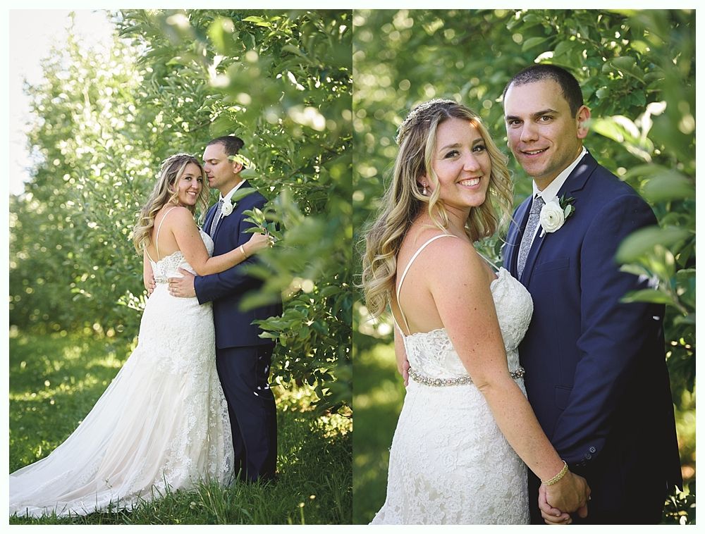 Bride and groom in wedding attire pose outdoors amidst greenery, smiling at the camera.