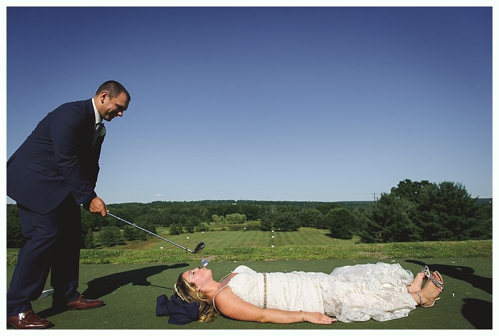 Groom putting golf ball while bride lies on green, wedding day, sunny outdoor setting.