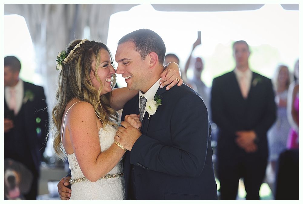Newly married couple laughing while dancing at outdoor wedding reception.