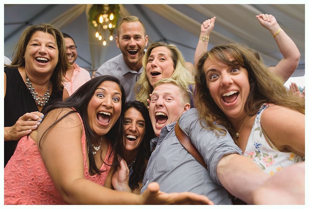 Group of people smiling and excited, taking a selfie inside a white tent at an event.