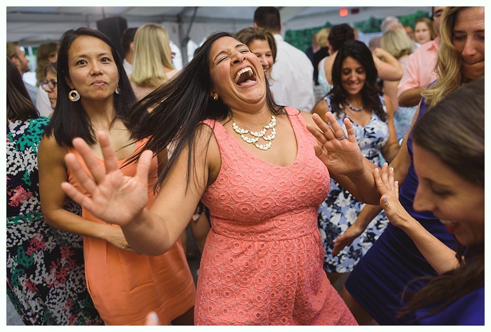 Woman in pink dress laughing and dancing with raised hands at an outdoor event.