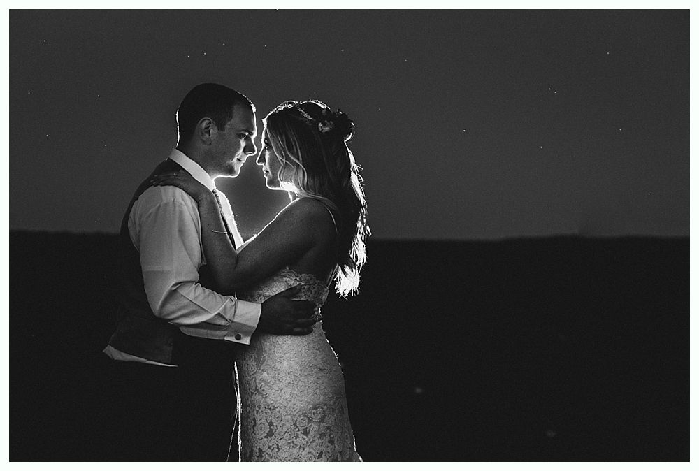 Bride and groom embrace in a silhouette; backlit, formal wear, intimate moment.