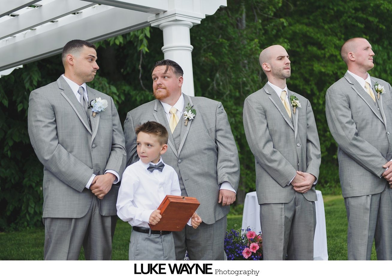 Men and a boy in gray suits stand at an outdoor wedding ceremony.