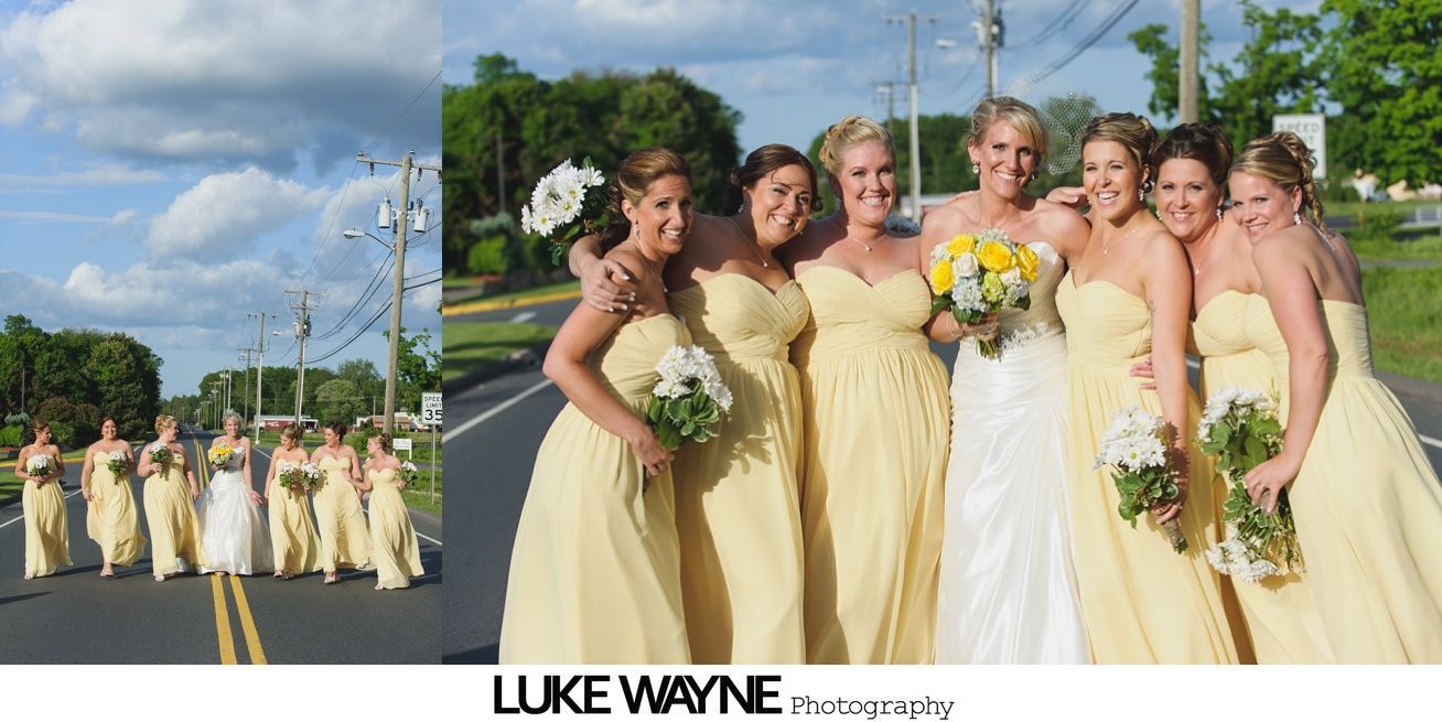 A bride and bridesmaids in yellow dresses pose on a road under a blue sky with fluffy clouds.