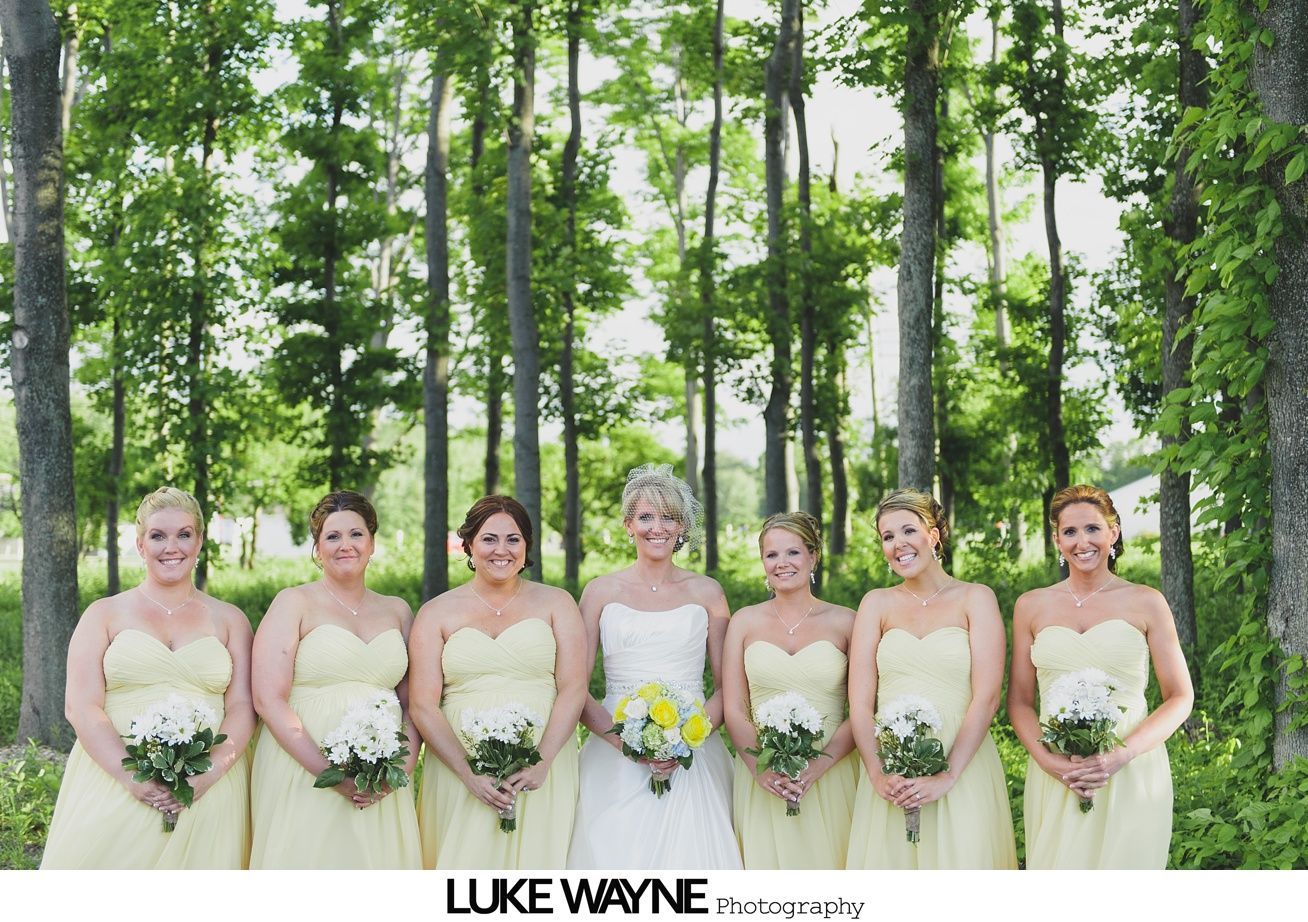 Bride and bridesmaids in yellow dresses holding bouquets pose in a forest.